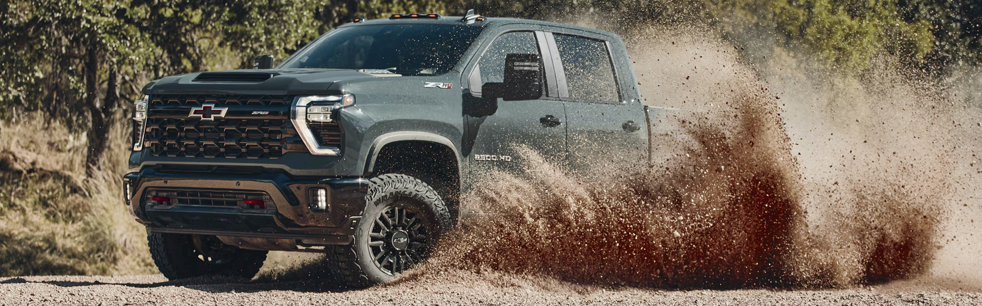Dark green Chevrolet Silverado HD ZR2 kicking up a cloud of dirt on a forest trail