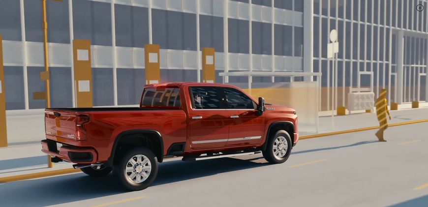 Red Chevrolet Silverado HD driving along a city street beside a construction barrier