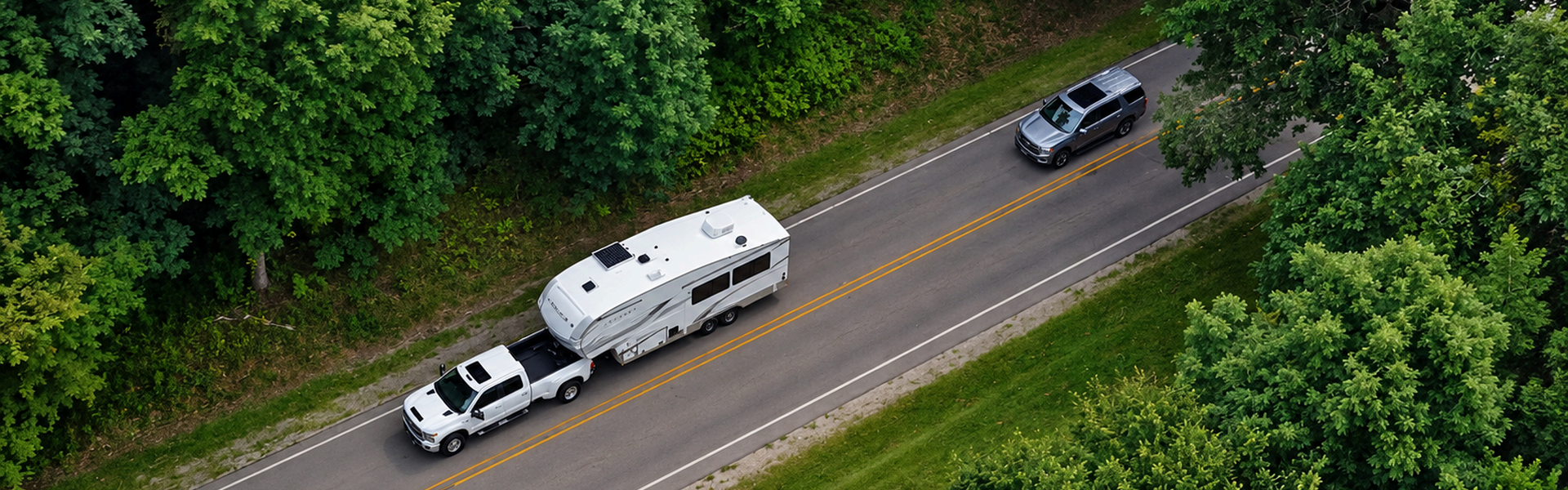Aerial view of a white Chevrolet Silverado HD towing a travel trailer down a tree-lined road