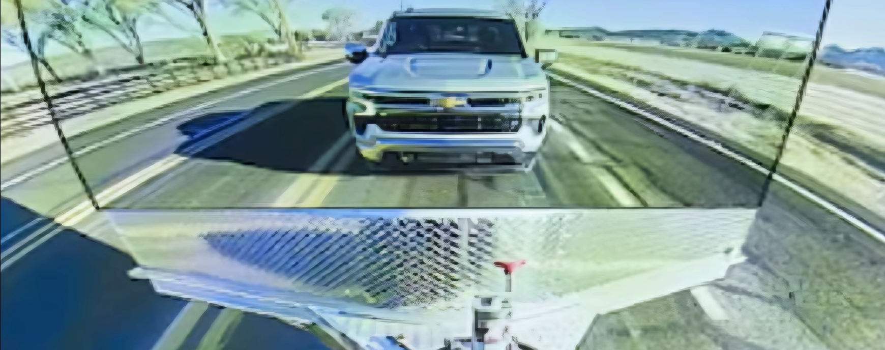 Transparent trailer camera view showing the road and a following truck through the trailer
