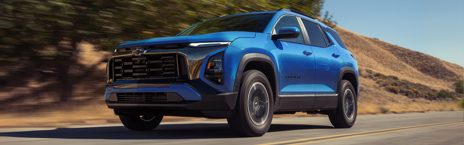 Blue 2027 Chevrolet Equinox driving along a road past a dry hillside