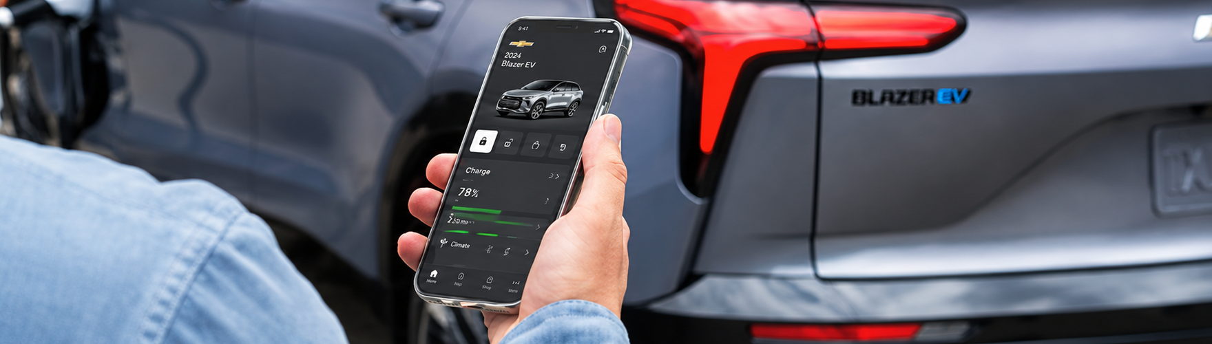 Hand holding a phone with the Chevrolet app open beside the taillamp of a Chevrolet Blazer EV