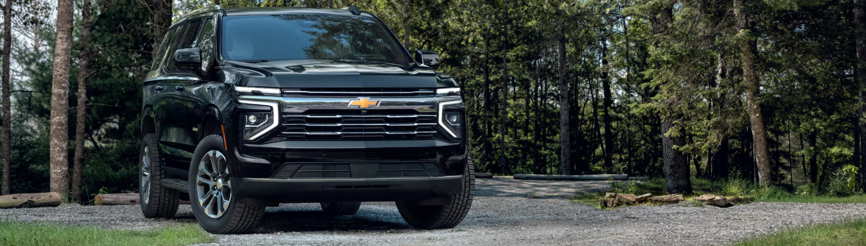 Black 2027 Chevrolet Tahoe parked on a gravel clearing in a pine forest
