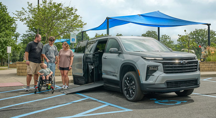 Family beside a silver BraunAbility Chevrolet Traverse with its side ramp lowered for a wheelchair user