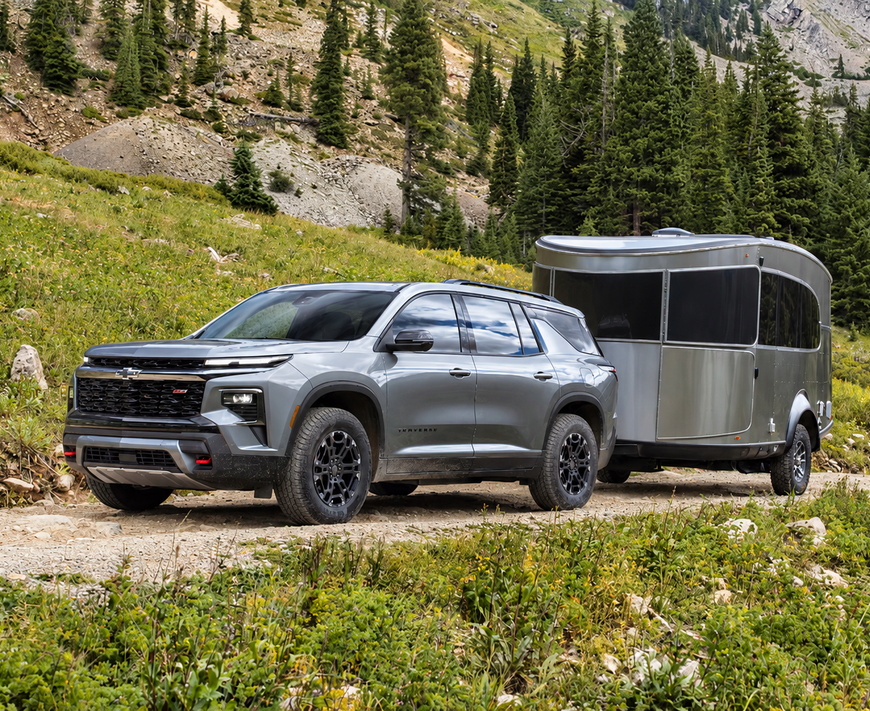Silver Chevrolet Traverse Z71 towing a camper trailer across a mountain meadow