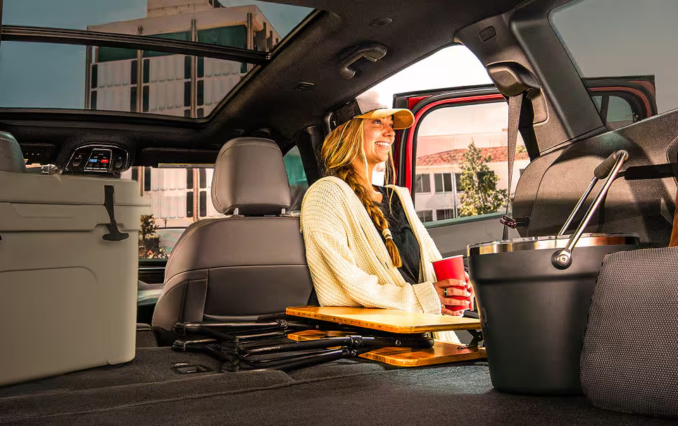 Woman enjoying a drink in the open cargo area of a 2027 Jeep Cherokee