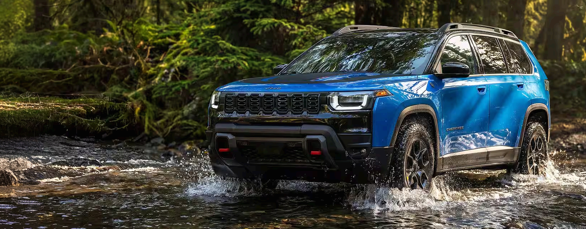 Blue 2027 Jeep Cherokee driving through a shallow forest stream