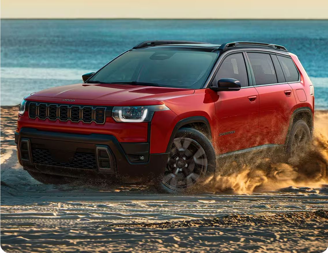 Red 2027 Jeep Cherokee kicking up sand on a beach
