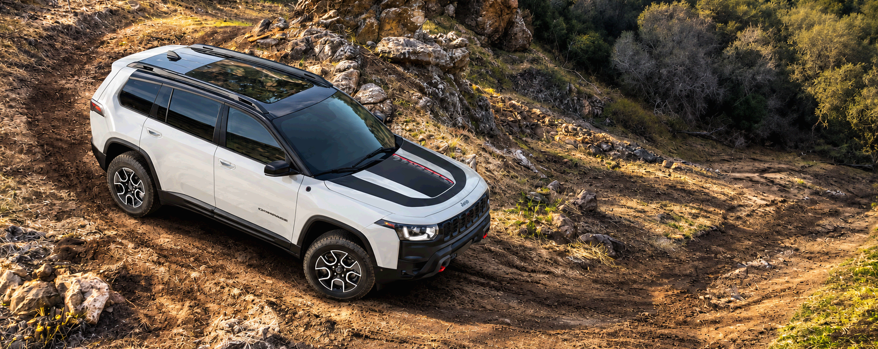 White 2027 Jeep Cherokee Trailhawk with a black hood decal climbing a rocky dirt trail