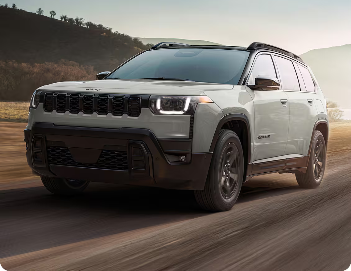 Silver 2027 Jeep Cherokee driving on a dirt road at sunrise