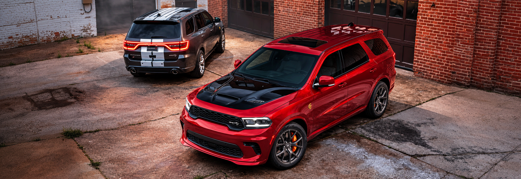 Red Dodge Durango with a black hood and a gray Durango with white racing stripes parked in a brick courtyard