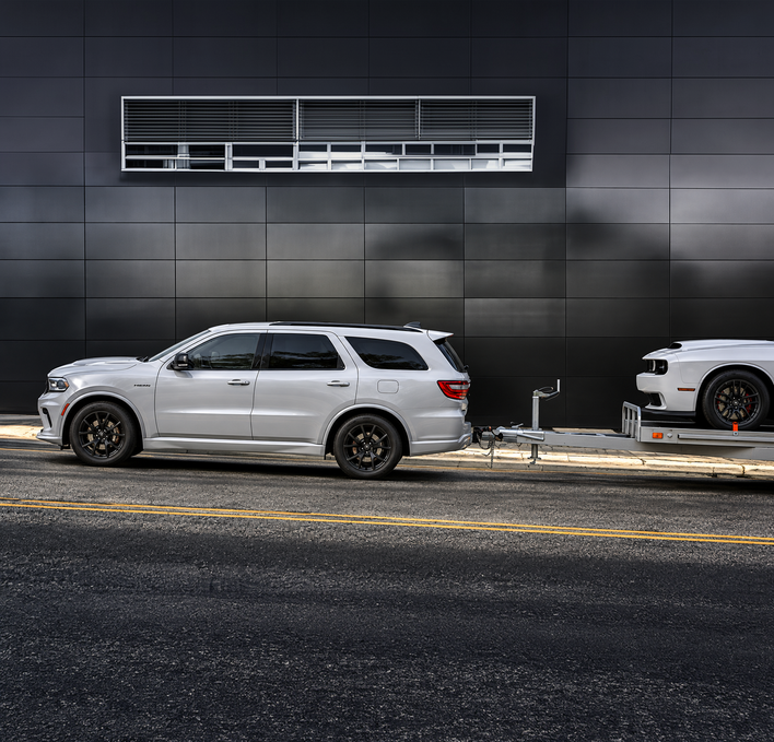White Dodge Durango with a trailer in front of a dark modern building