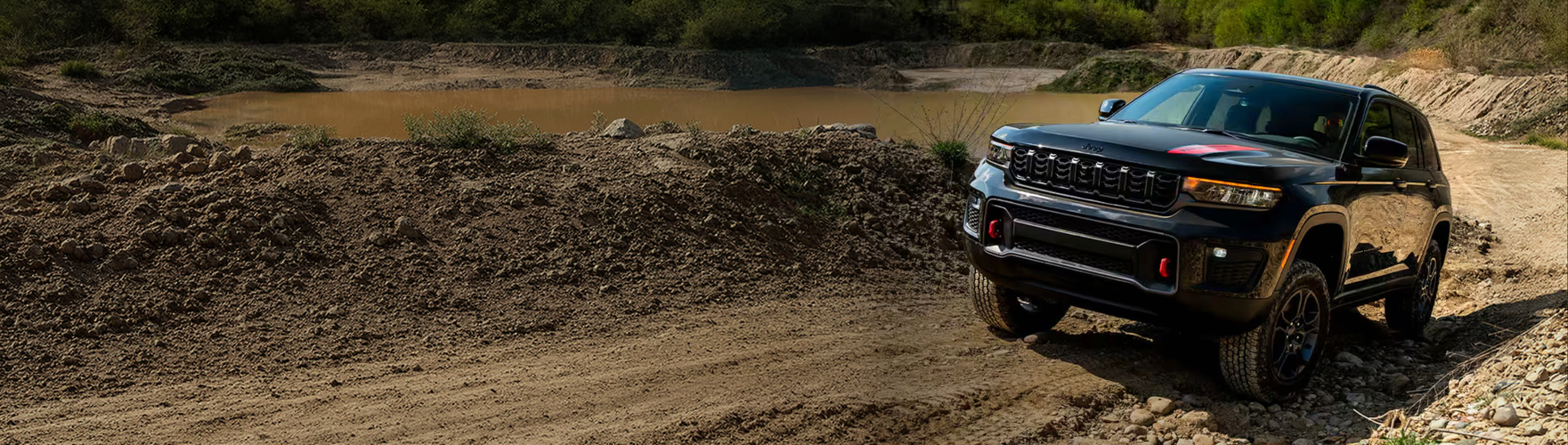 Black Grand Cherokee Trailhawk driving along a rocky dirt trail