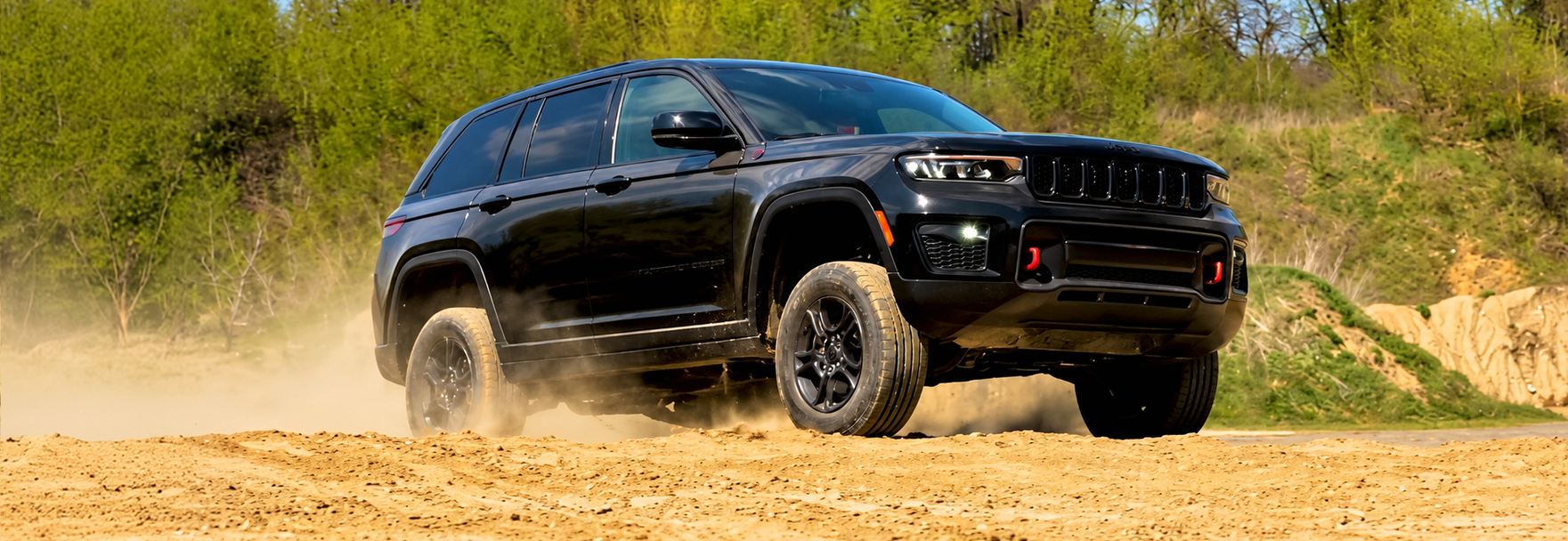 Black 2027 Jeep Grand Cherokee Trailhawk kicking up dust on a dirt track