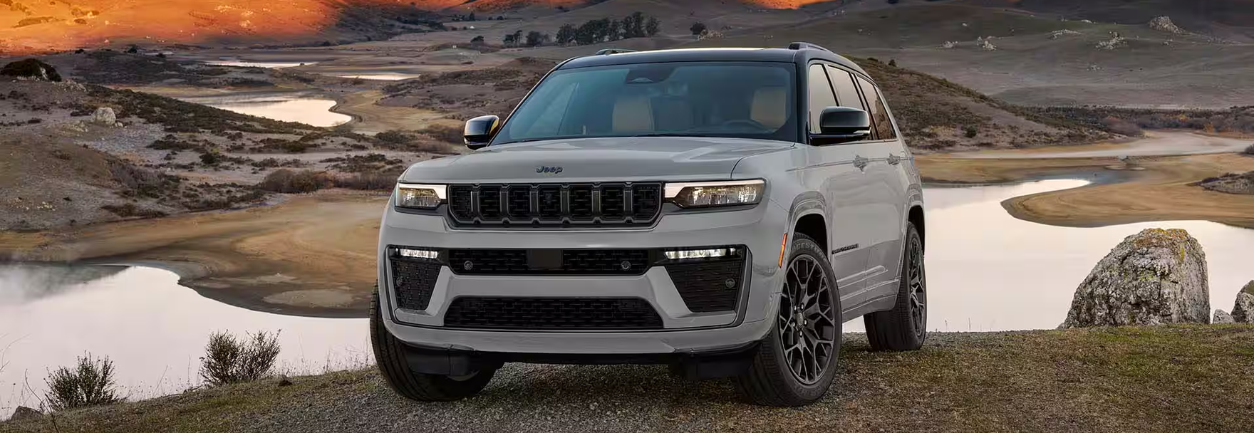 Silver Grand Cherokee L parked on a hillside above coastal tide pools at sunset