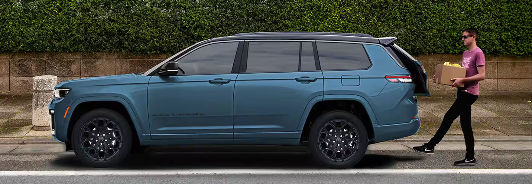 Man carrying a box toward the open liftgate of a blue Grand Cherokee L