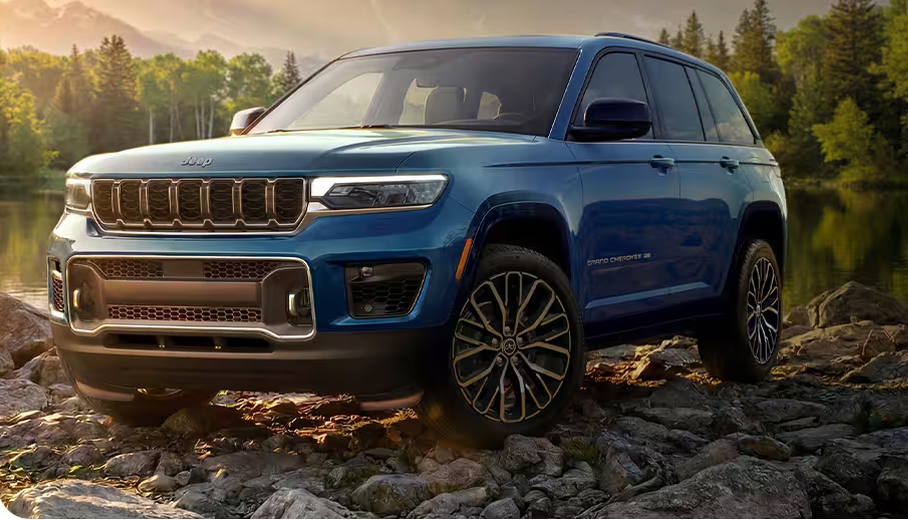 Blue 2027 Jeep Grand Cherokee Overland on rocks beside a forest lake
