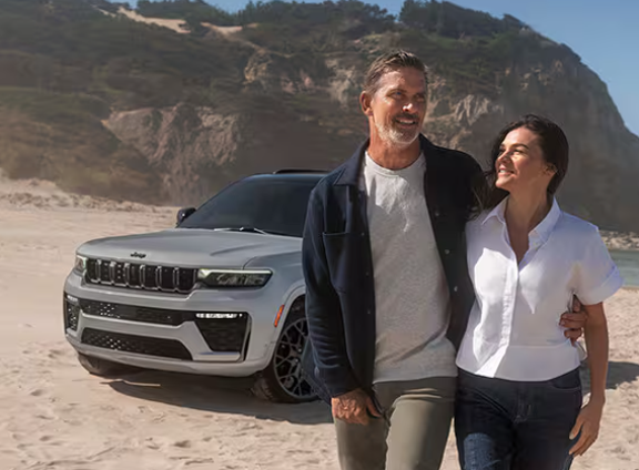 Couple walking on a beach in front of a silver Grand Cherokee