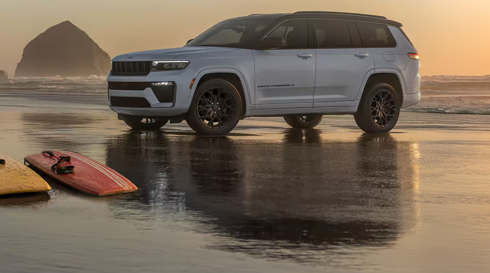 Silver Grand Cherokee L on a wet beach at sunset