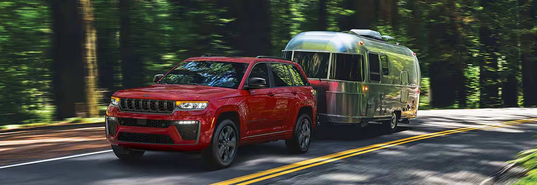 Red Grand Cherokee towing a silver travel trailer on a forest road