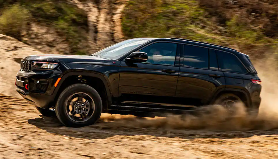 Black Grand Cherokee Trailhawk spraying sand as it drives up a dirt slope