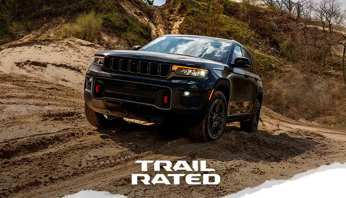 Black 2027 Jeep Grand Cherokee Trailhawk climbing a dirt trail with a Trail Rated badge