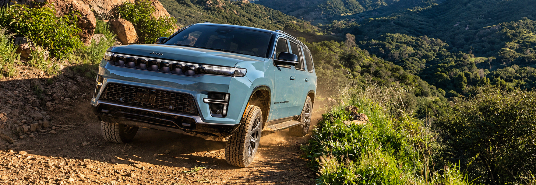 Light blue 2027 Jeep Grand Wagoneer climbing a rocky dirt trail in green hills