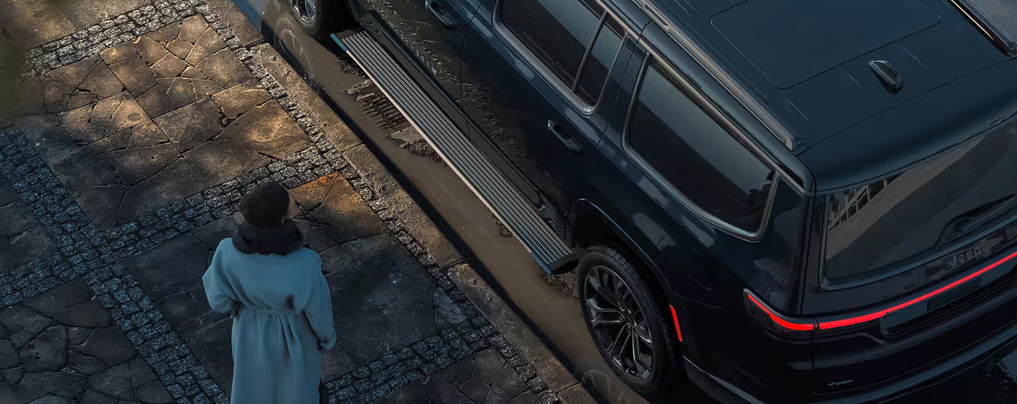 Overhead view of a person walking up to a black Grand Wagoneer with its power running board deployed