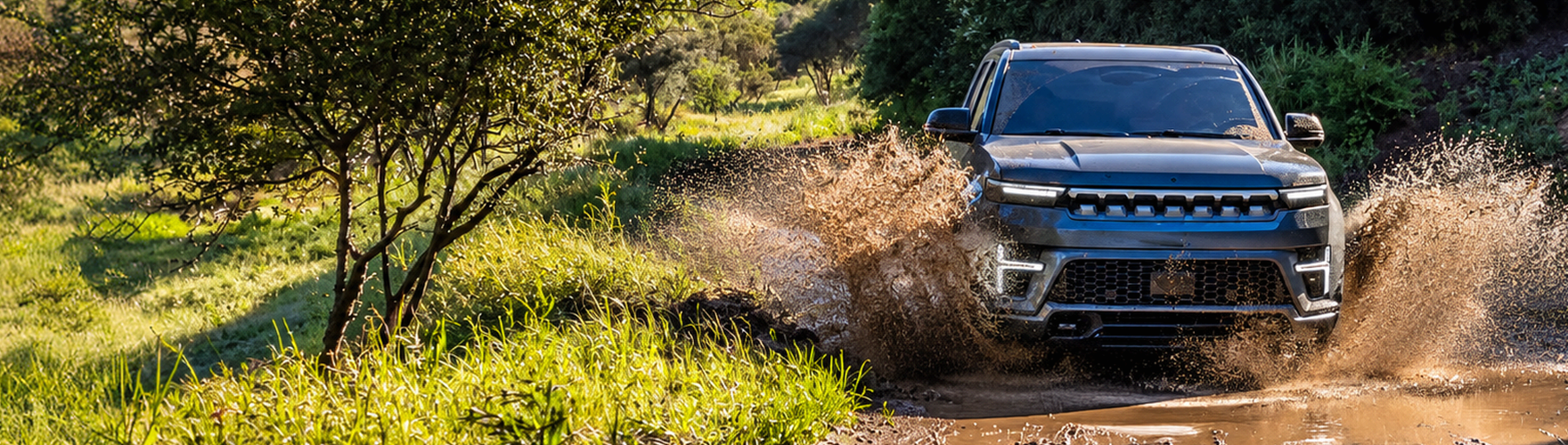 Blue 2027 Jeep Grand Wagoneer splashing through a muddy trail in a grassy field