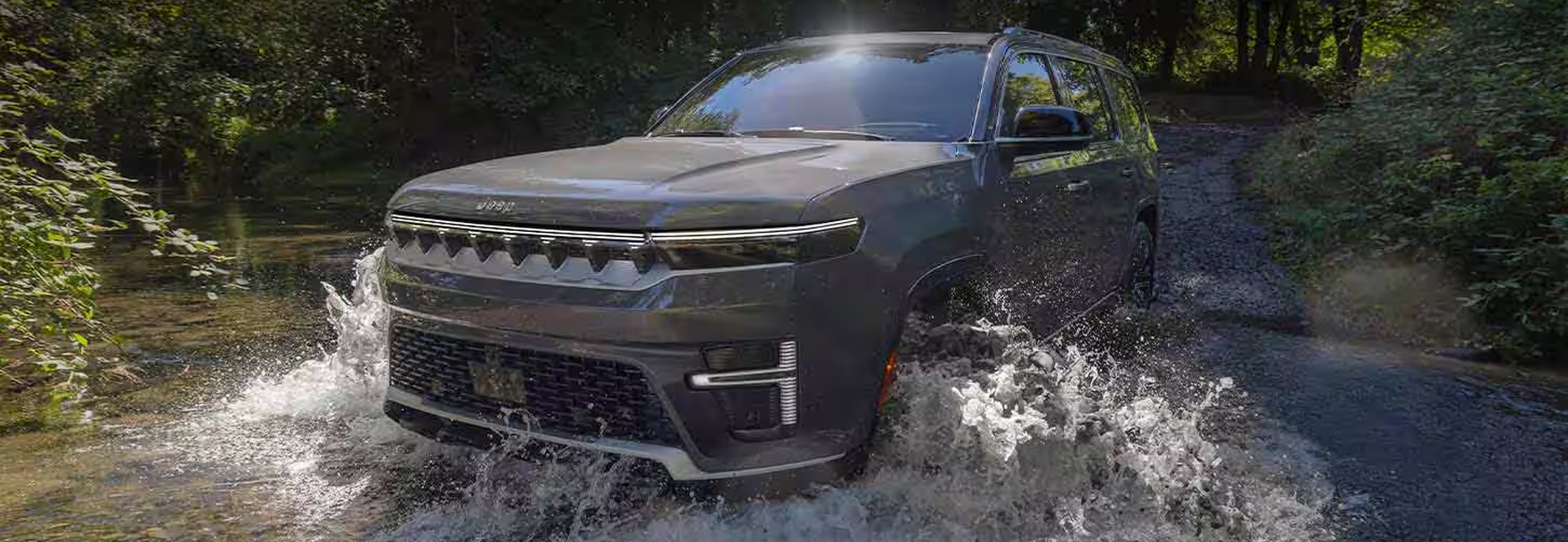 Dark gray 2027 Jeep Grand Wagoneer splashing through a forest stream