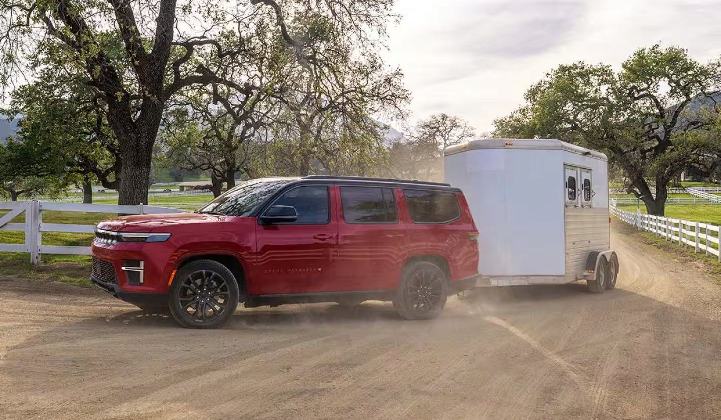 Red 2027 Jeep Grand Wagoneer towing a horse trailer on a dusty ranch road